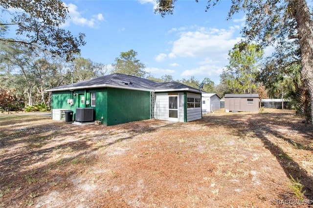 rear view of property with central air condition unit and a shed