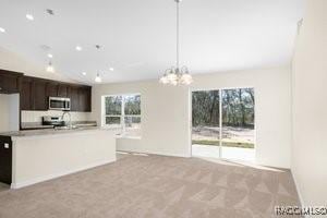 kitchen featuring light carpet, decorative light fixtures, an island with sink, a notable chandelier, and dark brown cabinets