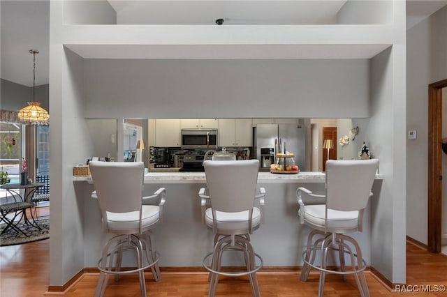 kitchen with light wood finished floors, a kitchen bar, light countertops, appliances with stainless steel finishes, and a peninsula