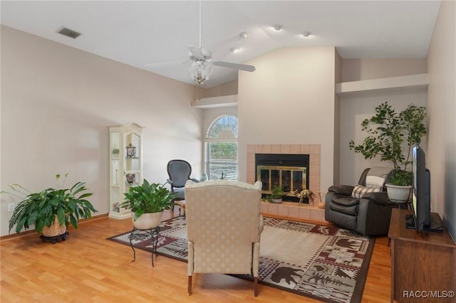 living room featuring a tiled fireplace, visible vents, a ceiling fan, and wood finished floors