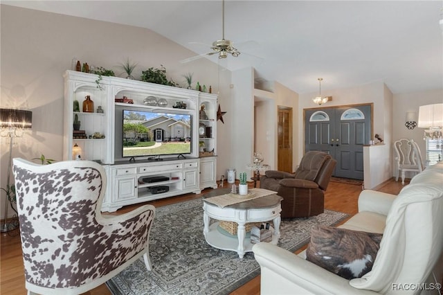 living area with ceiling fan with notable chandelier, light wood-type flooring, and lofted ceiling