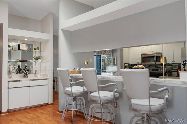 kitchen featuring stainless steel microwave, a kitchen breakfast bar, light countertops, and light wood-style floors