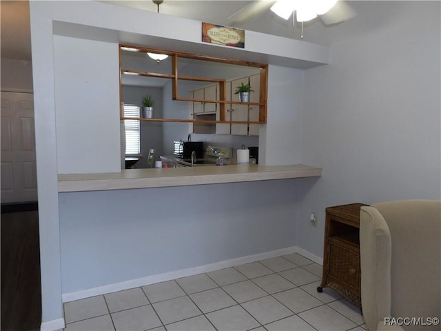 kitchen featuring light tile patterned floors, baseboards, black microwave, and light countertops