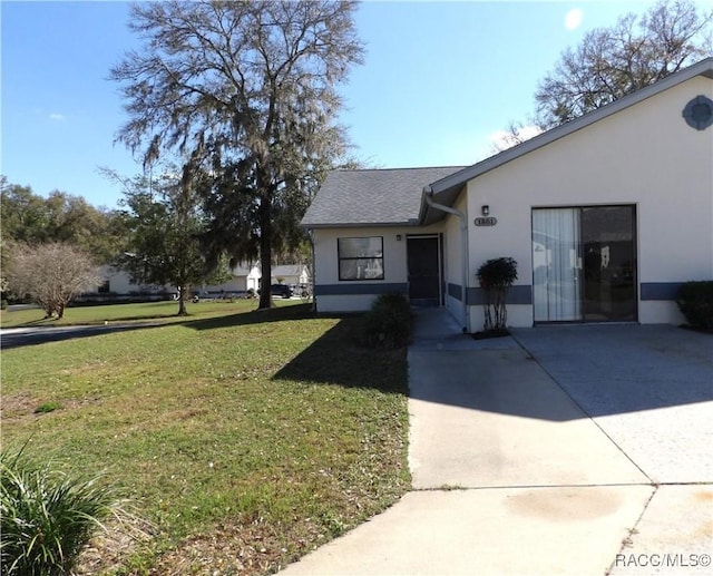 view of front of property featuring roof with shingles, a front lawn, and stucco siding