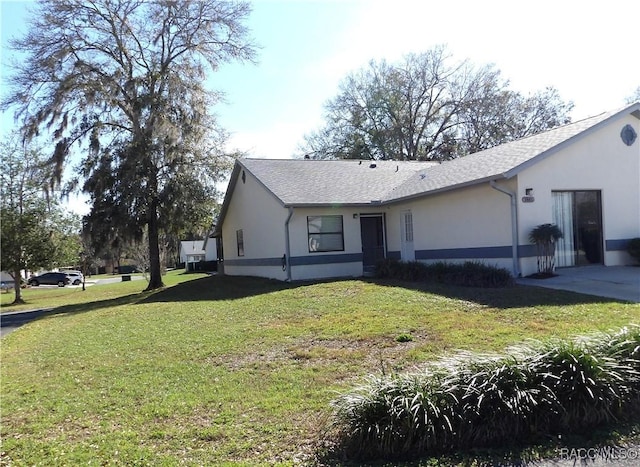 view of front facade featuring roof with shingles, a front lawn, and stucco siding