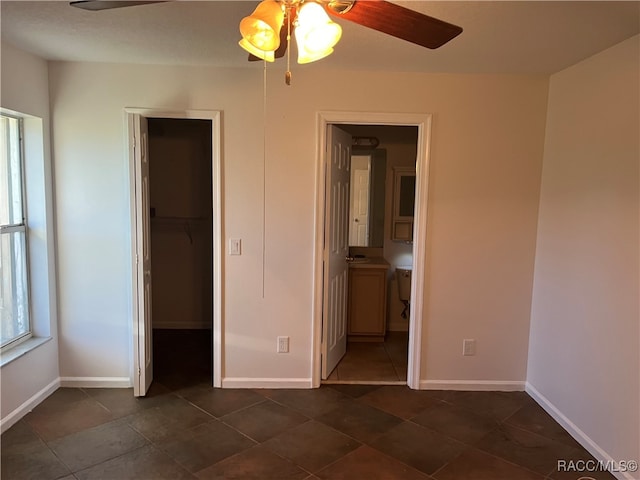 unfurnished bedroom featuring ensuite bathroom, a walk in closet, ceiling fan, dark tile patterned floors, and a closet