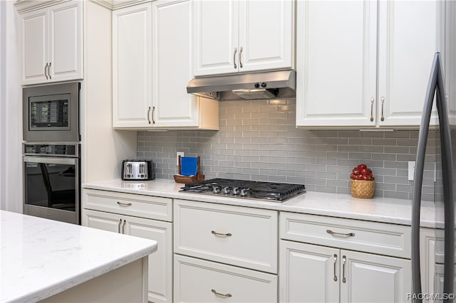 kitchen featuring tasteful backsplash, light stone countertops, white cabinets, and appliances with stainless steel finishes