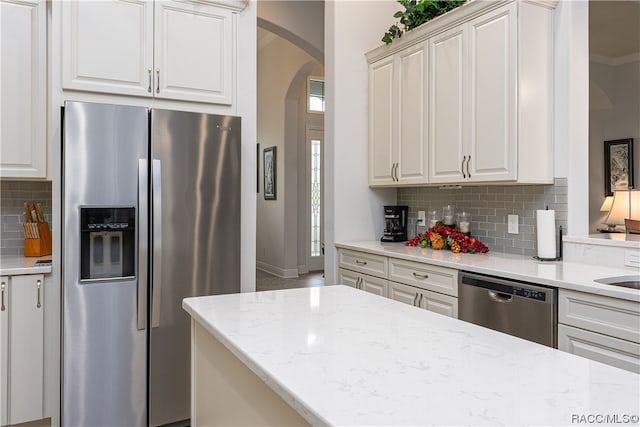 kitchen with appliances with stainless steel finishes, tasteful backsplash, light stone counters, and crown molding