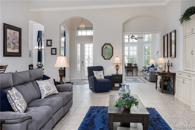 tiled living room with crown molding, a high ceiling, and ceiling fan with notable chandelier