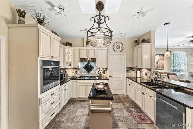 kitchen featuring appliances with stainless steel finishes, a sink, a ceiling fan, stone finish flooring, and backsplash