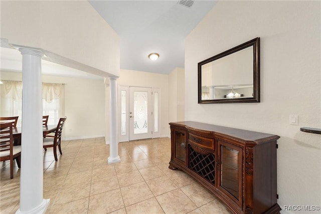 foyer featuring lofted ceiling, light tile patterned floors, and ornate columns