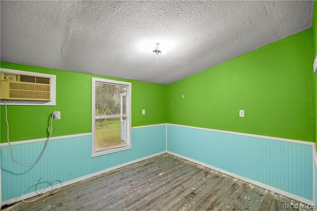 unfurnished room featuring an AC wall unit, hardwood / wood-style floors, and a textured ceiling