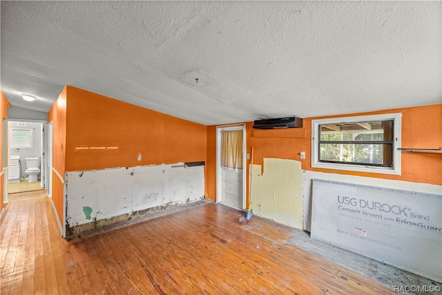 unfurnished room featuring hardwood / wood-style floors, lofted ceiling, and a textured ceiling