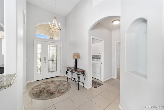 tiled entryway with washing machine and clothes dryer, a high ceiling, and an inviting chandelier