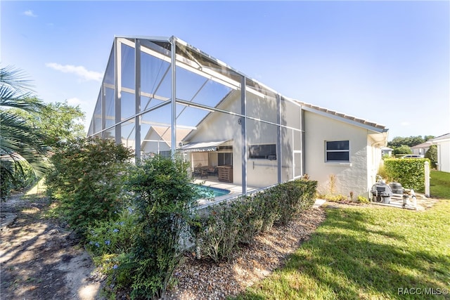 back of house with glass enclosure, a patio area, and a yard