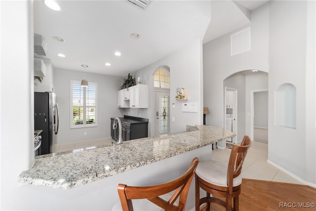 kitchen with kitchen peninsula, a breakfast bar, pendant lighting, white cabinets, and stainless steel refrigerator