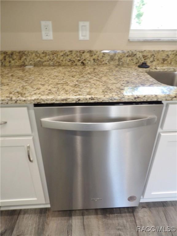 room details featuring stainless steel dishwasher, light stone countertops, white cabinetry, and dark wood-type flooring