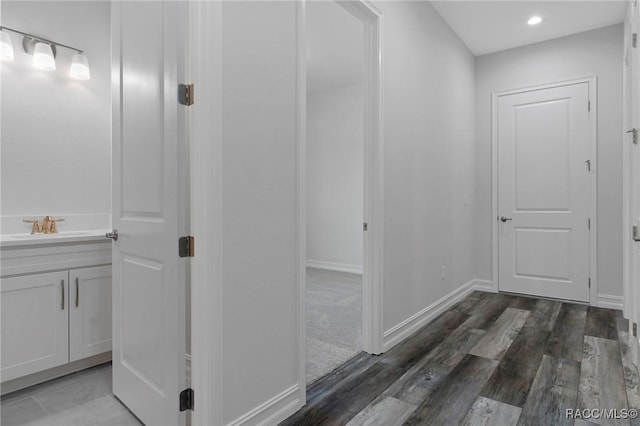 hallway featuring a sink, recessed lighting, wood finished floors, and baseboards