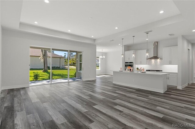 unfurnished living room featuring dark wood-type flooring, a tray ceiling, and baseboards