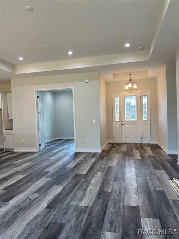 entryway with an inviting chandelier, dark wood-type flooring, and a tray ceiling