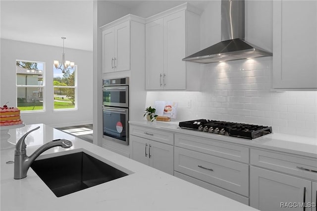 kitchen featuring decorative backsplash, wall chimney exhaust hood, appliances with stainless steel finishes, white cabinetry, and a sink