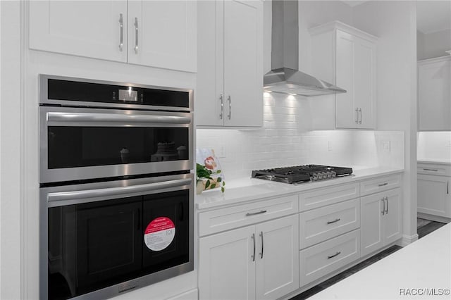 kitchen with white cabinets, light countertops, appliances with stainless steel finishes, decorative backsplash, and wall chimney exhaust hood