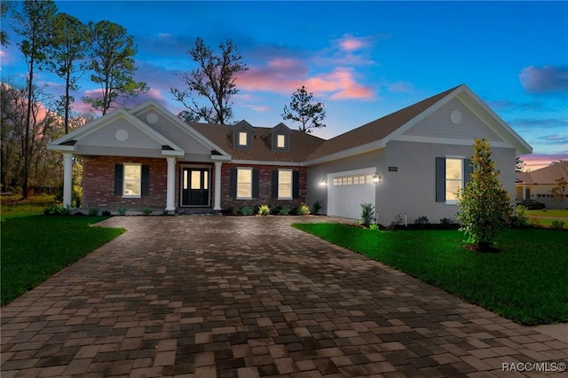 view of front of house featuring a garage, decorative driveway, brick siding, and a yard