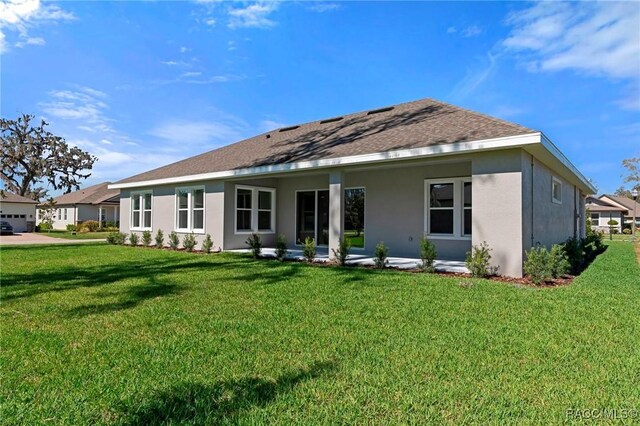 rear view of property featuring stucco siding, a shingled roof, a patio, and a yard