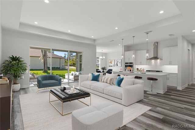 living room with a tray ceiling, recessed lighting, wood finished floors, and a notable chandelier