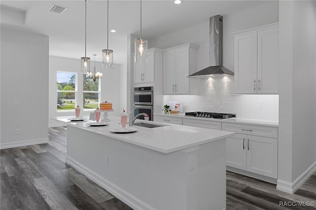 kitchen featuring gas stovetop, backsplash, double oven, white cabinetry, and wall chimney range hood