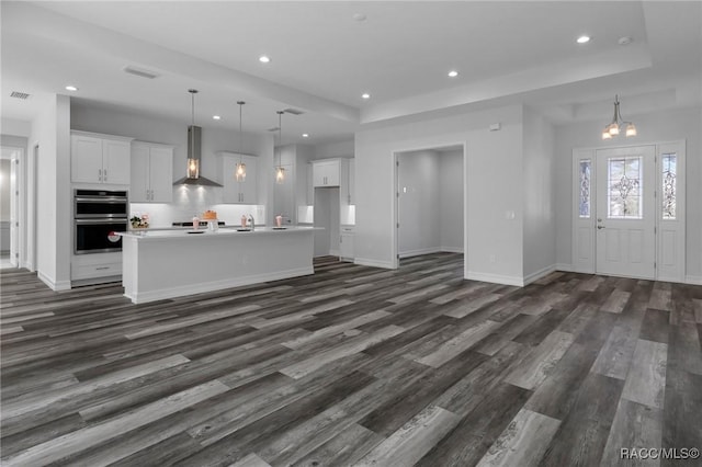 unfurnished living room featuring dark wood-type flooring, recessed lighting, a raised ceiling, and visible vents