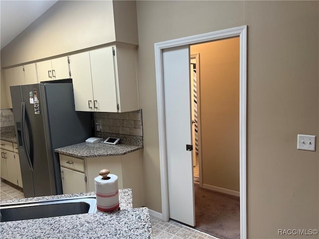 kitchen featuring light colored carpet, decorative backsplash, white cabinets, black fridge with ice dispenser, and lofted ceiling