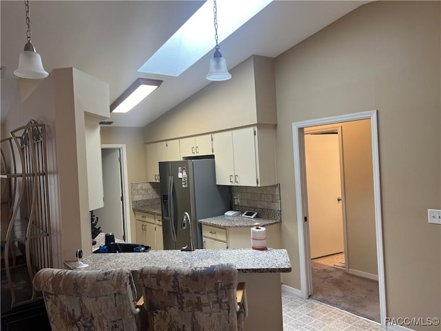 kitchen featuring stainless steel fridge with ice dispenser, lofted ceiling with skylight, hanging light fixtures, and decorative backsplash