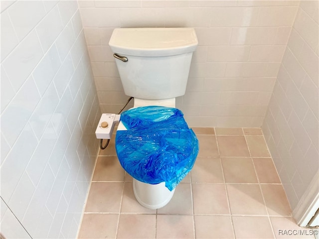 bathroom featuring toilet, tile patterned floors, and tile walls