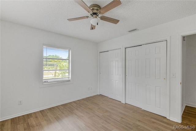 unfurnished bedroom with multiple closets, light wood-style flooring, visible vents, and a textured ceiling