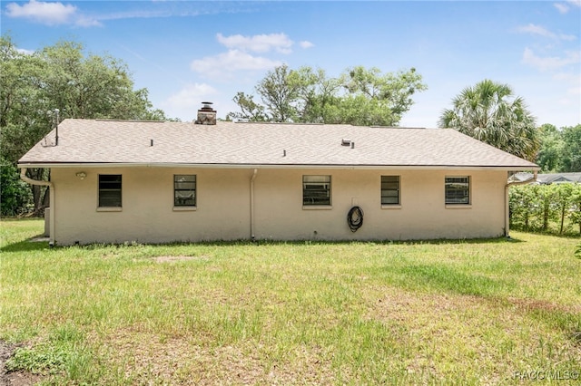rear view of property with a chimney, a yard, and stucco siding