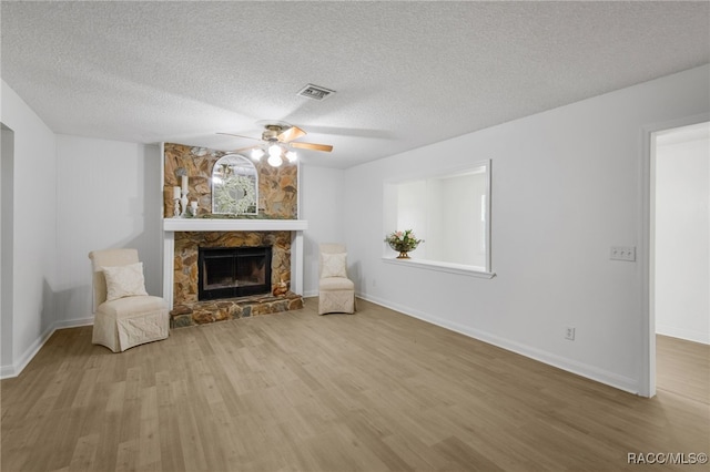 unfurnished living room featuring a ceiling fan, a fireplace, visible vents, and wood finished floors