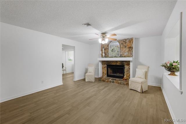 living room with wood finished floors, a textured ceiling, visible vents, a ceiling fan, and a stone fireplace