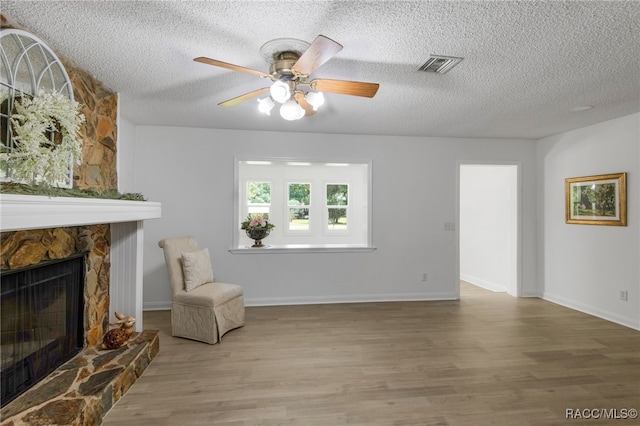 living area featuring wood finished floors, a textured ceiling, visible vents, a fireplace, and ceiling fan