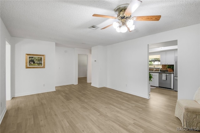 unfurnished living room with a textured ceiling, baseboards, ceiling fan, visible vents, and light wood-style floors