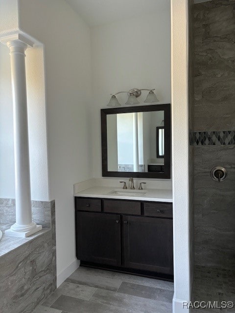 bathroom featuring decorative columns, vanity, and a tile shower