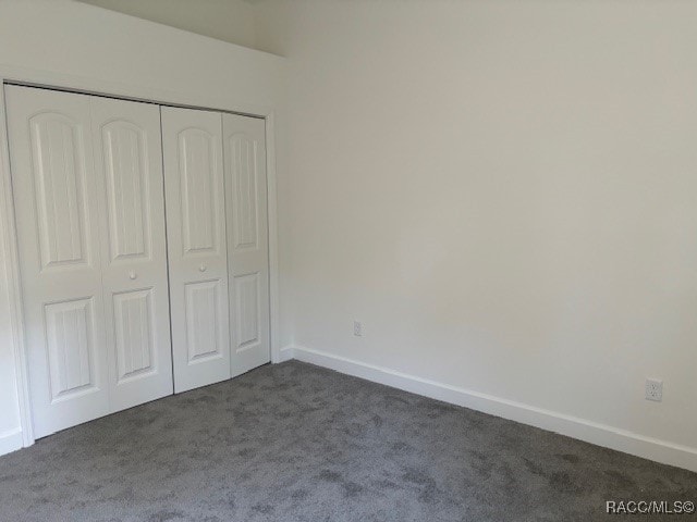 unfurnished bedroom with a closet and dark colored carpet