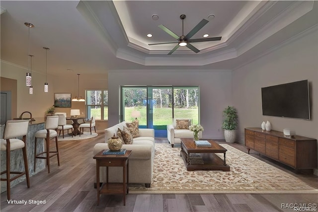 living room featuring hardwood / wood-style floors, ceiling fan, ornamental molding, and a tray ceiling