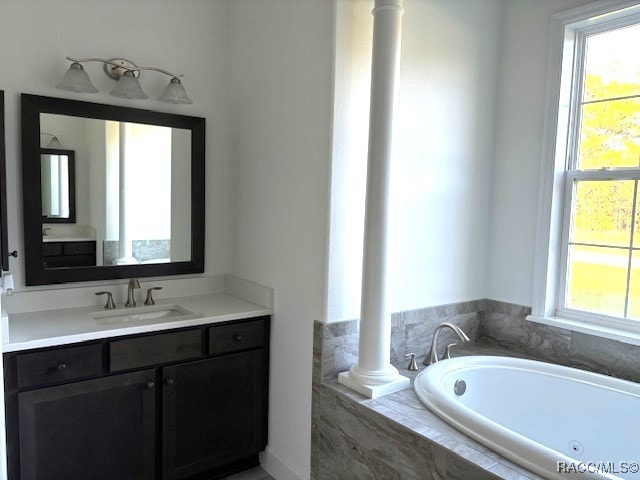 bathroom with ornate columns, vanity, and a relaxing tiled tub