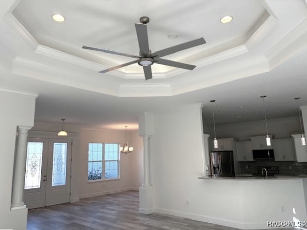 unfurnished living room with ceiling fan with notable chandelier, a tray ceiling, hardwood / wood-style flooring, and crown molding