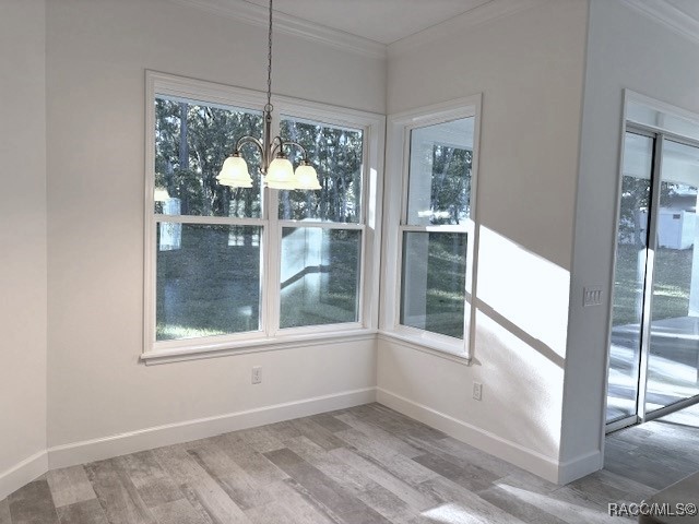 unfurnished dining area with hardwood / wood-style floors, crown molding, and an inviting chandelier