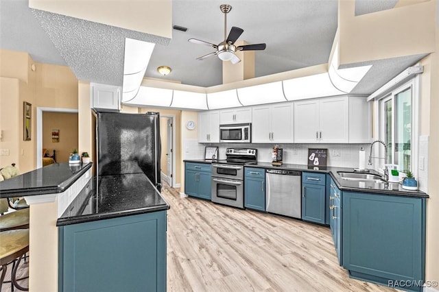 kitchen with dark countertops, appliances with stainless steel finishes, blue cabinets, white cabinetry, and a sink