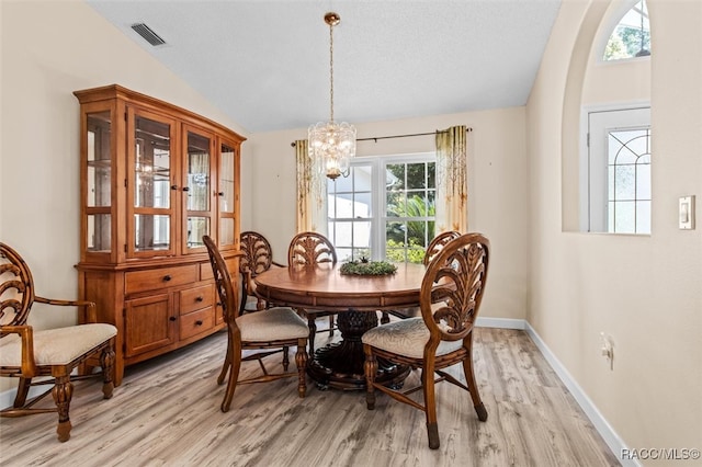 dining space with light hardwood / wood-style floors, lofted ceiling, a textured ceiling, and an inviting chandelier