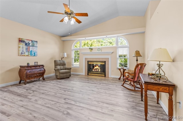 living area with a tile fireplace, light hardwood / wood-style floors, vaulted ceiling, and ceiling fan