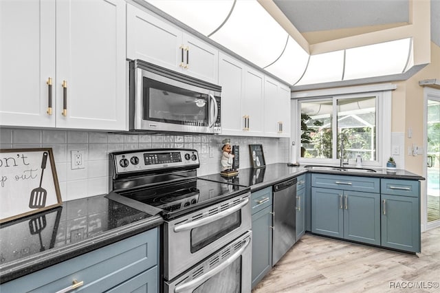 kitchen featuring light wood-type flooring, stainless steel appliances, vaulted ceiling, dark stone countertops, and white cabinetry